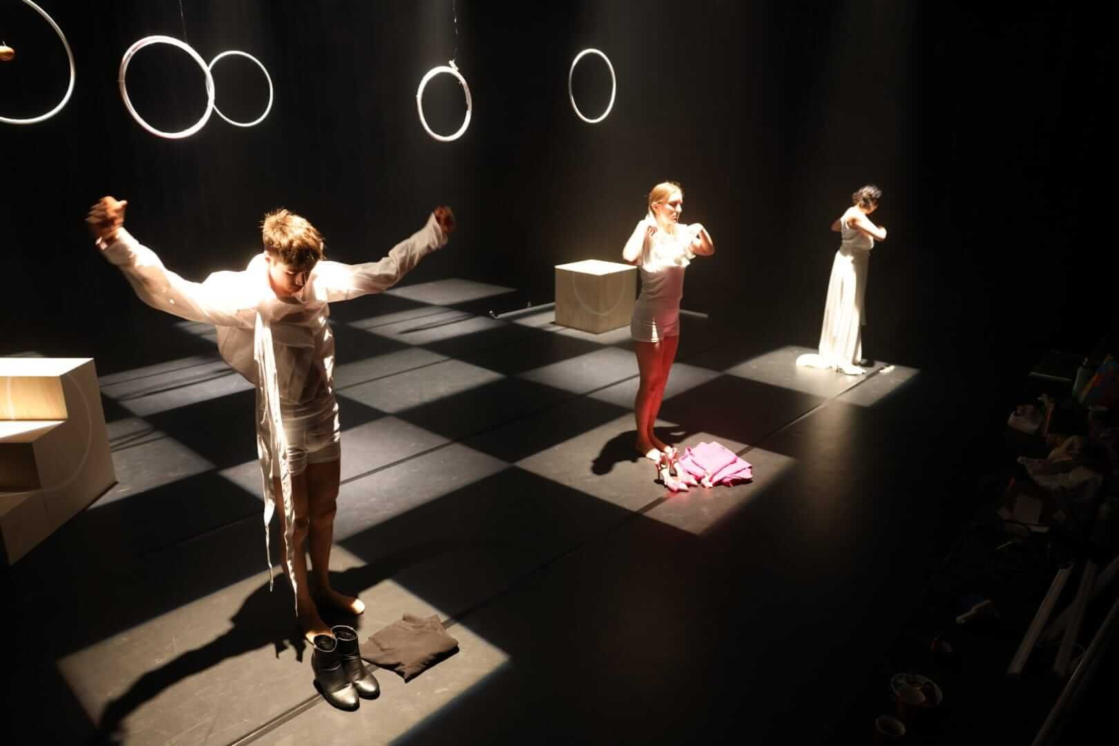 Stage with 3 actors on it all in there own light square getting dressed.